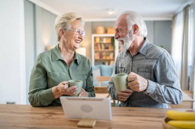 Kıdemli çift, Kafkasyalı yaşlı adam ve kadın, karı koca, emekli, büyükbaba ve büyükanne dijital tablet kullanıyor, aydınlık odada kahve içiyor, gerçek insanlar, aile kavramı, günlük rutin işler.