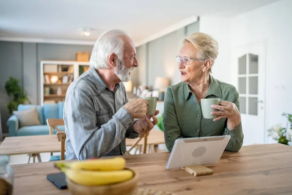 老夫老妻白种人老夫老妻养恤金领取者爷爷和奶奶在家里用数码平板电脑在明亮的房间里喝杯咖啡实人家庭日常观念 — 图库照片