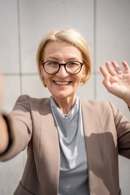 Kafkasyalı yetişkin bir iş kadınının portresi. Sarışın ve gözlüklü kadın. Gündüz vakti modern binanın beyaz duvarının önünde duruyor.