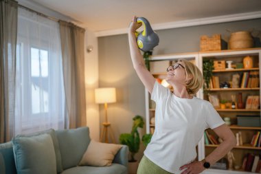 Evde kettlebell Girya Rus çanıyla antrenman yapan olgun bir beyaz kadın. Dairesinde sağlıklı yaşam tarzı kavramında kadın egzersizi yapıyor.