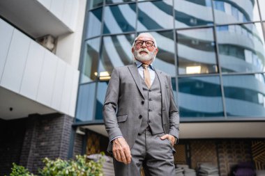 Takım elbiseli kıdemli işadamının portresi modern inşaat şirketinin önünde duruyor.