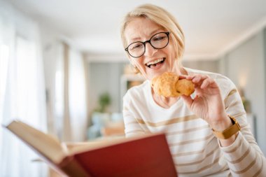Bir kadın olgun beyaz kadın aydınlık odada modern kitap okuyor gözlük takıyor gerçek bir insan mekanı kopyalıyor.
