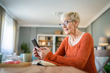 Yetişkin, sarışın, beyaz, son sınıf öğrencisi bir kadın dijital tablet kullanarak internet üzerinden sohbet ediyor.