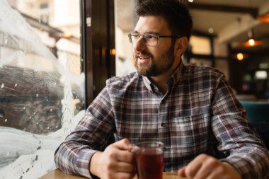 Adult caucasian man sitting alone at cafe front view of one male with beard and eyeglasses holding a cup of tea real people copy space