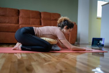 Yetişkin bir Kafkasyalı kadın evde restoratif yoga yapıyor.