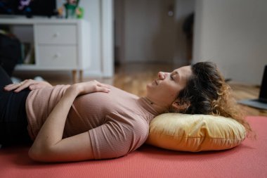 Yetişkin bir Kafkasyalı kadın evde restoratif yoga yapıyor.