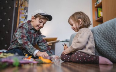 Small caucasian boy and girl siblings brother and sister children play at home sit on the floor at home childhood development growing up concept copy space domestic life