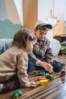 Small caucasian boy and girl siblings brother and sister children play at home sit on the floor at home childhood development growing up concept copy space domestic life