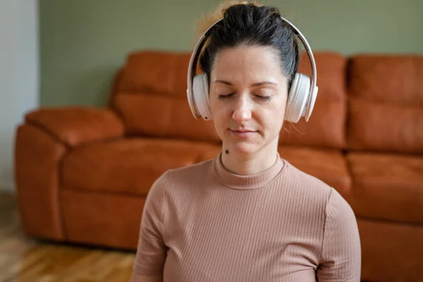 1人の女性大人白人女性ミレニアル世代オンラインガイド付き瞑想のためのヘッドフォンを使用してマインドフルネスヨガを練習自宅で床の上に目を閉じて本物の人々のセルフケアコンセプトコピースペース — ストック写真