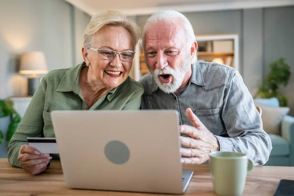 一对成熟的老年男女坐在家里用信用卡或借记卡上网购物浏览网店买东西用笔记本电脑真人复制空间 — 图库照片