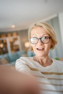 Evde gözlüklü, olgun, beyaz bir kadının portresi mutlu bir gülümseme ile kameraya bakıyor parlak oda kullanıcısı tarafından oluşturulan içerik portresi çirkin fotokopi alanı içinde kazak giyiyor.