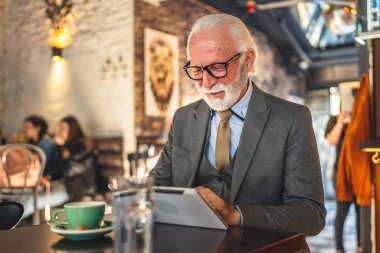 Bir üst düzey Kafkas erkek iş adamı Kafe 'de dijital tablet kullanıyor. Kıyafet fotokopi alanı kullanıyor.