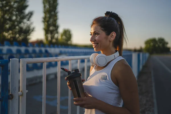 stock image One woman adult caucasian millennial female standing on stadium on the race track after or before training taking a brake hold supplement shaker bottle of water healthy lifestyle concept copy space