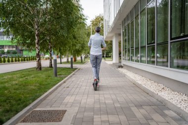 Yetişkin, yaşlı, beyaz bir kadın. Elektrikli scooterın üzerinde duruyor. Kasabada ya da şehirde araba sürüyor.