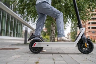 Bilinmeyen bir kadının ayakları kenarda duruyor ya da şehirde ya da kasabada, çevre dostu modern bir taşımacılıkta, kaldırımda elektrikli scooter kullanıyor.