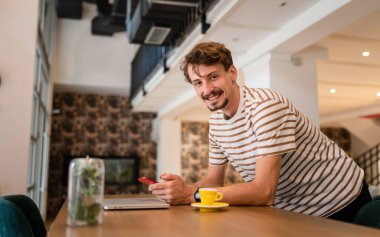 one caucasian man young adult millennial male using mobile phone stand at table in cafe at the table alone happy smile confident having online chat using internet for text messages or social network