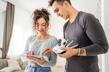 Young couple man and woman husband and wife or caucasian boyfriend and girlfriend setting up home surveillance security camera cctv protecting their home apartment bright room real people copy space