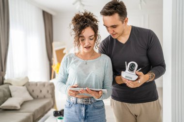 Young couple man and woman husband and wife or caucasian boyfriend and girlfriend setting up home surveillance security camera cctv protecting their home apartment bright room real people copy space