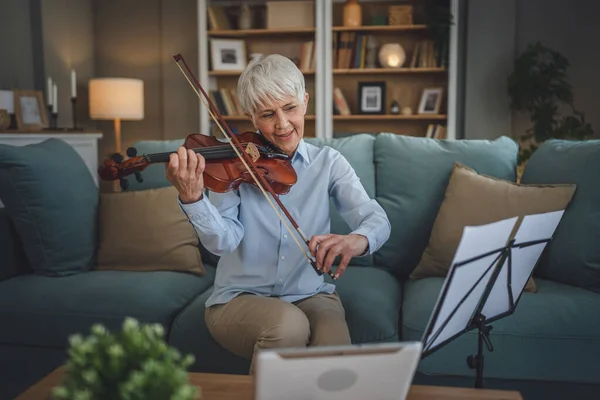 成熟したシニア白人女性は自宅でバイオリンの練習をすることを学ぶオンライン教授の先生は教えるか 自宅でソファベッドの上に座っている間 デジタルタブレット上でインターネットプライベートクラスを持っていますアクティブシニア趣味 — ストック写真