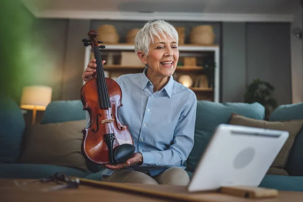 成熟したシニア白人女性は自宅でバイオリンの練習をすることを学ぶオンライン教授の先生は教えるか 自宅でソファベッドの上に座っている間 デジタルタブレット上でインターネットプライベートクラスを持っていますアクティブシニア趣味 — ストック写真
