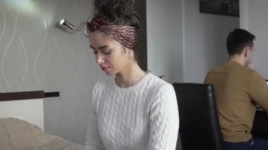 Beyaz bir kadın otel odasında bavuldan kıyafetlerini çıkarırken kocası ya da erkek arkadaşı arka planda oturup mutlu bir gülümseme seyahati ve tatil konseptini kopyalarken.