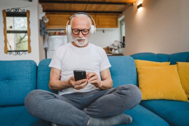 Kulaklıklı bir son sınıf öğrencisi evde müzik dinlemek için smsrtphone kullanıyor.