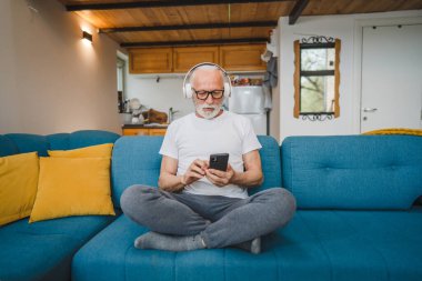 Kulaklıklı bir son sınıf öğrencisi evde müzik dinlemek için smsrtphone kullanıyor.