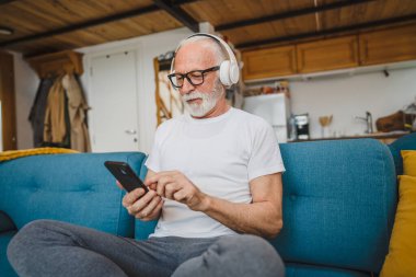 Kulaklıklı bir son sınıf öğrencisi evde müzik dinlemek için smsrtphone kullanıyor.