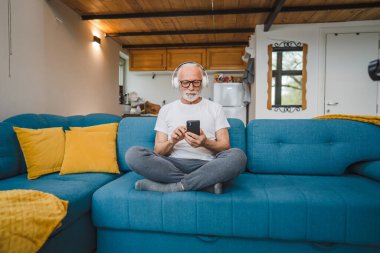 Kulaklıklı bir son sınıf öğrencisi evde müzik dinlemek için smsrtphone kullanıyor.