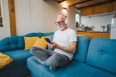 Kulaklıklı bir son sınıf öğrencisi evde müzik dinlemek için smsrtphone kullanıyor.