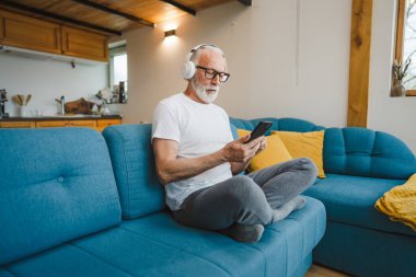 Kulaklıklı bir son sınıf öğrencisi evde müzik dinlemek için smsrtphone kullanıyor.