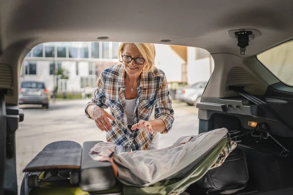 一个成熟的金发美女旅行理念女性在搬家或到达目的地时 会从她的车后部拿走一些东西 — 图库照片