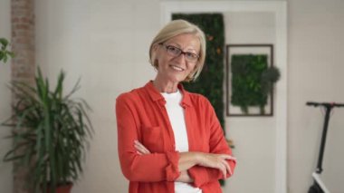 Evde ya da işyerinde gözlüklü, mutlu gülümseyen ve kameraya bakan olgun sarışın bir kadının portresi. Yavaş çekimde kendine güvenen süveter giy.