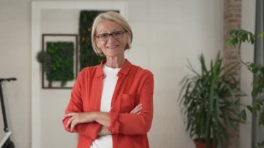 Evde ya da işyerinde gözlüklü, mutlu gülümseyen ve kameraya bakan olgun sarışın bir kadının portresi. Yavaş çekimde kendine güvenen süveter giy.