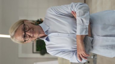 Evde ya da işyerinde gözlüklü, mutlu gülümseyen ve kameraya bakan olgun sarışın bir kadının portresi. Yavaş çekimde kendine güvenen süveter giy.