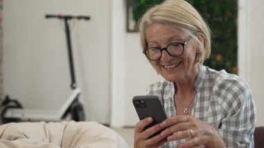 Yetişkin, beyaz, sarışın bir kadın cep telefonu akıllı telefonu kullanarak mesaj atıyor. Mutlu, kendine güvenen, gerçek, ağır çekimde insanlar.