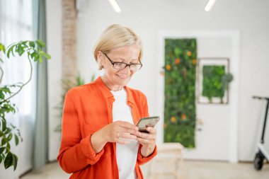 Yetişkin, beyaz, sarışın bir kadın cep telefonu akıllı telefonu kullanarak mesaj atıyor. Mutlu, kendine güvenen, gerçek insanlar uzayı kopyalıyor.