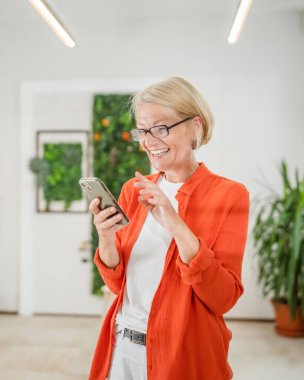 Yetişkin, beyaz, sarışın bir kadın cep telefonu akıllı telefonu kullanarak mesaj atıyor. Mutlu, kendine güvenen, gerçek insanlar uzayı kopyalıyor.