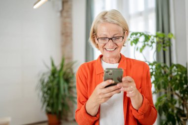 Yetişkin, beyaz, sarışın bir kadın cep telefonu akıllı telefonu kullanarak mesaj atıyor. Mutlu, kendine güvenen, gerçek insanlar uzayı kopyalıyor.