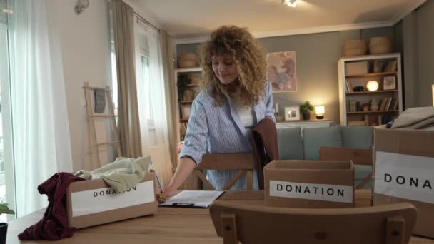 여성은 곱슬머리의 코카서스 여성으로 집에서 기부를 의상을 준비하고 상자에 물건을 — 비디오