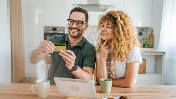 Couple caucasian man and woman husband and wife or boyfriend and girlfriend use laptop computer and credit card shopping online buy stuff or pay make payment e-commerce from home real people
