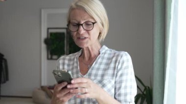 Yetişkin, beyaz, sarışın bir kadın cep telefonu akıllı telefonu kullanarak mesaj atıyor. Mutlu, kendine güvenen, gerçek, ağır çekimde insanlar.