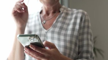 Yetişkin, beyaz, sarışın bir kadın cep telefonu akıllı telefonu kullanarak mesaj atıyor. Mutlu, kendine güvenen, gerçek, ağır çekimde insanlar.