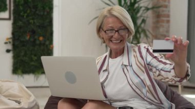 Yetişkin bir kadın evde oturup online alışveriş için kredi kartı ya da banka kartı kullanıyor. İnternetten alışveriş yapıyor, bir şeyler alıyor. Dizüstü bilgisayar kullanıyor.