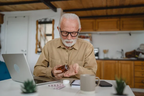 stock image One senior man caucasian male grandfather sit at home hold pack of drug tablet painkillers or vitamin supplement read label ready to take medicine near laptop order online copy space