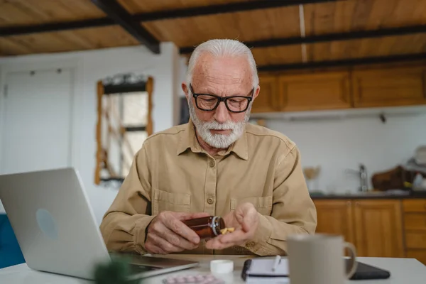 一位高年级的男性祖父坐在家里 手里拿着一包药丸 止痛药或维生素补充剂 准备吃药 — 图库照片