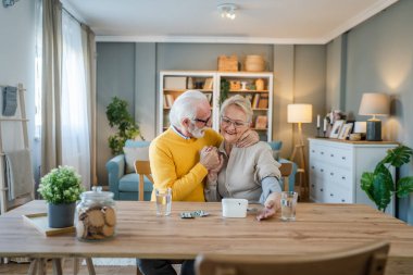 Üst düzey çift kadın kan basıncını ölçerken kocası beyaz adam evde masada oturuyor gerçek insanlar aile yaşlıları emeklilik ve sağlık konsepti