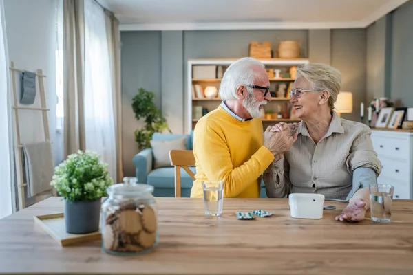 年长的夫妇女人检查血压 而她的丈夫 年长的高加索男人坐在桌旁真正的人家庭老人退休和健康的概念 — 图库照片