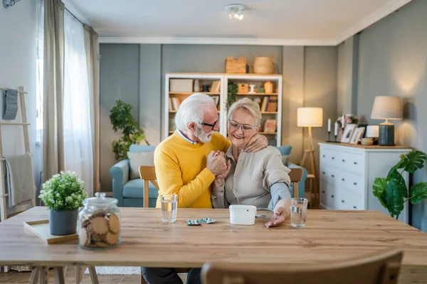 年长的夫妇女人检查血压 而她的丈夫 年长的高加索男人坐在桌旁真正的人家庭老人退休和健康的概念 — 图库照片