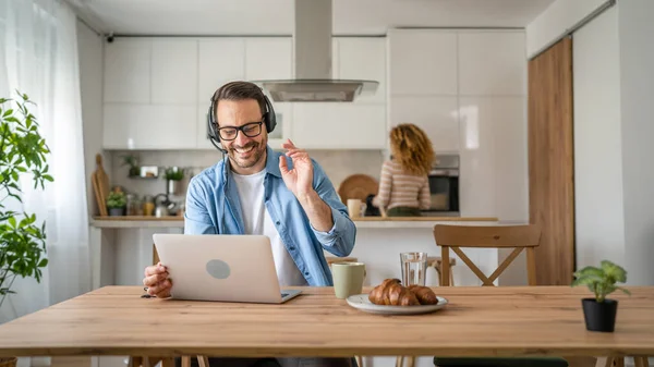 一名男子在家里工作 头上戴着耳机 头戴手提电脑 他笑得很开心 相信妻子会站在他的后面 — 图库照片